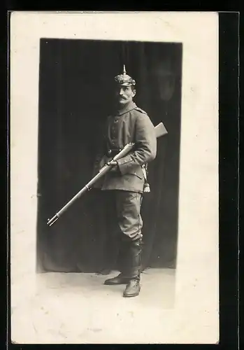 Foto-AK preussishcer Soldat in Feldgrau Uniform mit Pickelhaube und Gewehr, Ledergamaschen