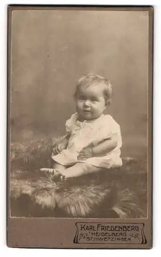 Fotografie Karl Friedenberg, Heidelberg, Portrait niedliches Kleinkind im weissen Hemd auf Fell sitzend