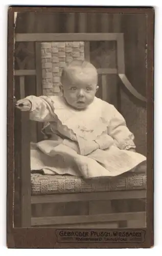 Fotografie Gebrüder Pfusch, Wiesbaden, Portrait niedliches Baby im hübschen Kleid auf Stuhl sitzend
