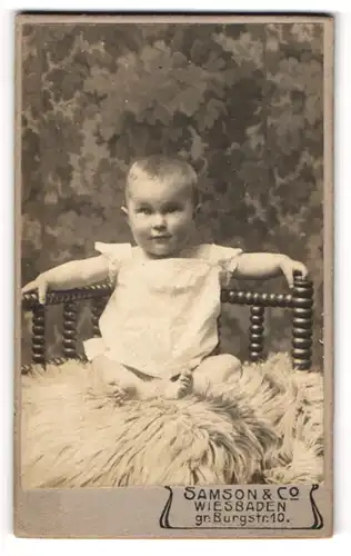 Fotografie Samson & Co., Wiesbaden, Portrait niedliches Baby im weissen Hemd auf Fell sitzend