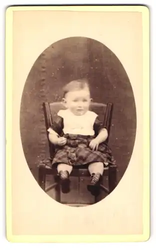 Fotografie unbekannter Fotograf und Ort, Portrait niedliches Klelinkind im karierten Kleid auf Stuhl sitzend