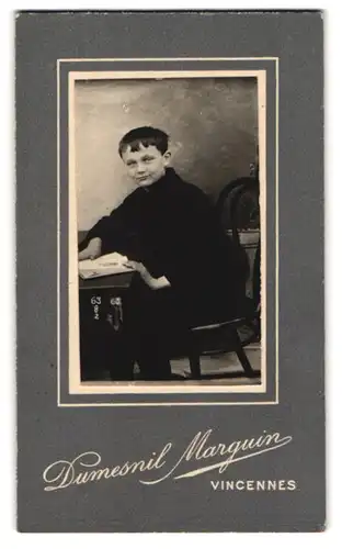 Fotografie Dumesnil Marguin, Vincennes, Portrait schwarz gekleideter Junge mit Buch am Tisch sitzend