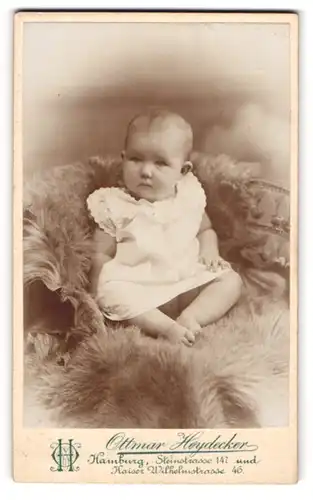 Fotografie Ottmar Heydecker, Hamburg, Portrait niedliches Baby im weissen Hemd auf Fell sitzend