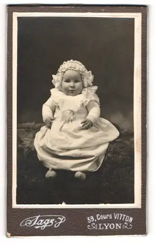 Fotografie A. Sage, Lyon, Portrait süsses Baby im Rüschenkleidchen und Schleifenmütze