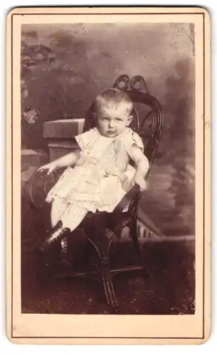 Fotografie unbekannter Fotograf und Ort, Portrait niedliches Kleinkind im weissen Kleid auf Stuhl sitzend