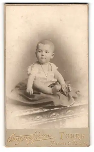 Fotografie Duguay Géran, Tours, Portrait niedliches Baby im weissen Hemd auf Decke sitzend