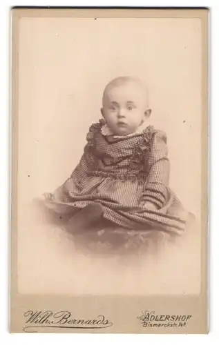 Fotografie Wilh. Bernards, Adlershof, Portrait niedliches Baby im karierten Kleid auf Tisch sitzend