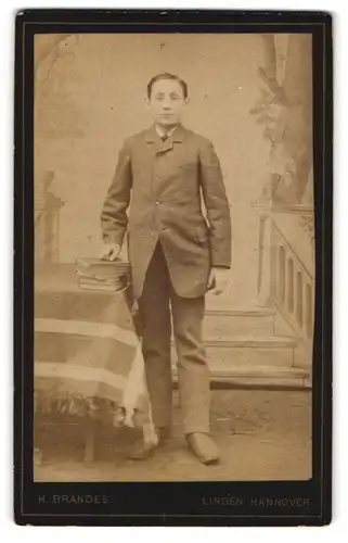 Fotografie H. Brandes, Hannover-Linden, Portrait junger Mann im Anzug mit Büchern an Tisch gelehnt