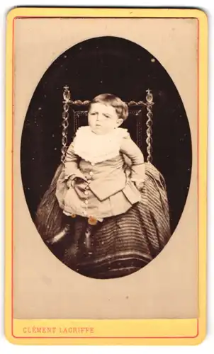 Fotografie Clément Lagriffe, Paris, Portrait niedliches Kleinkind im hübschen Kleid mit Latz auf Stuhl sitzend
