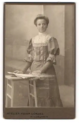 Fotografie Heinr. Cordes, Hildesheim, Portrait bürgerliche Dame mit Zeitung an Tisch gelehnt
