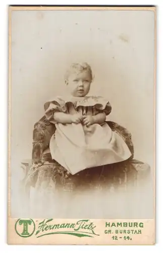 Fotografie Hermann Tietz, Hamburg, Portrait niedliches Kleinkind im hübschen Kleid auf Sessel sitzend