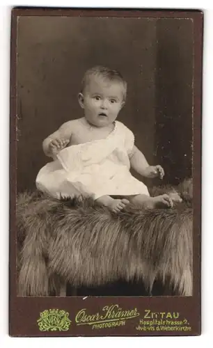 Fotografie Oscar Krämer, Zittau, Portrait niedliches Kleinkind im weissen Hemd auf Fell sitzend