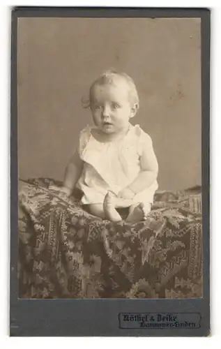 Fotografie Nöthel & Deike, Hannover-Linden, Portrait niedliches Kleinkind im weissen Hemd auf Decke sitzend