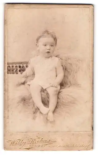 Fotografie Willy Kabus, Minden i / Westf., Portrait niedliches Kleinkind im weissen Hemd auf Fell sitzend