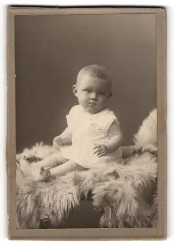 Fotografie unbekannter Fotograf und Ort, Portrait niedliches Kleinkind im weissen Hemd auf Fell sitzend