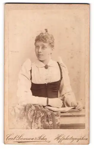 Fotografie Carl Siemsen & Sohn, Lübeck, Portrait junge Dame in modischer Kleidung mit Kragenbrosche und Buch
