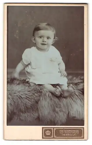 Fotografie Heinrich Schmorrde, Herrnhut, Portrait niedliches Kleinkind im weissen Hemd auf Fell sitzend