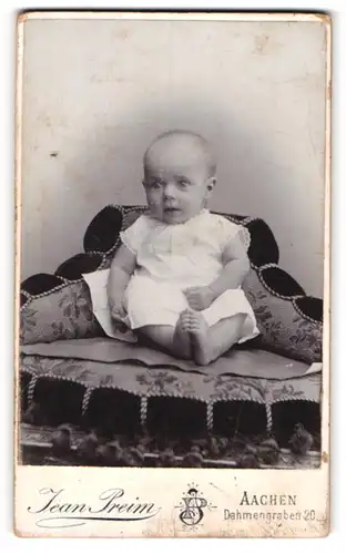 Fotografie Jean Preim, Aachen, Portrait niedliches Baby im weissen Hemd mit nackigen Füssen