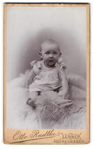 Fotografie Otto Radtke, Lennep, Portrait niedliches Baby im weissen Hemd auf Fell sitzend