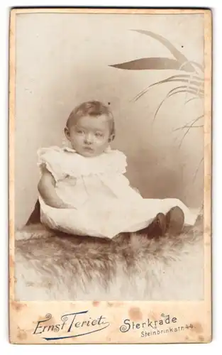 Fotografie Ernst Teriet, Sterkrade, Portrait niedliches Baby im weissen Hemd auf Fell sitzend