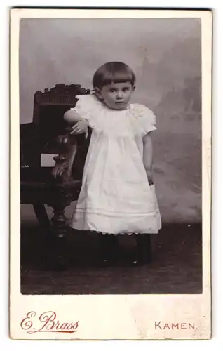 Fotografie Ernst Brass, Kamen, Portrait kleines Mädchen im weissen Kleid an Stuhl gelehnt