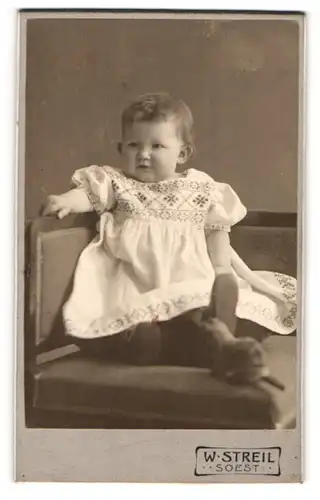 Fotografie W. Streil, Soest, Portrait niedliches Kleinkind im hübschen Kleid mit Spieltier