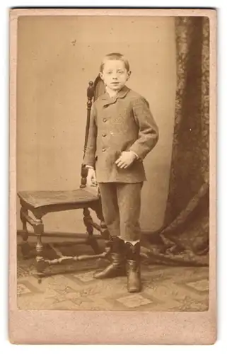 Fotografie unbekannter Fotograf und Ort, Portrait kleiner Junge im Anzug vor Stuhl stehend