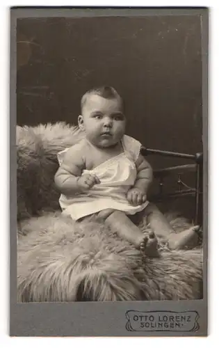 Fotografie Otto Lorenz, Solingen, Portrait niedliches Kleinkind im weissen Hemd auf Fell sitzend
