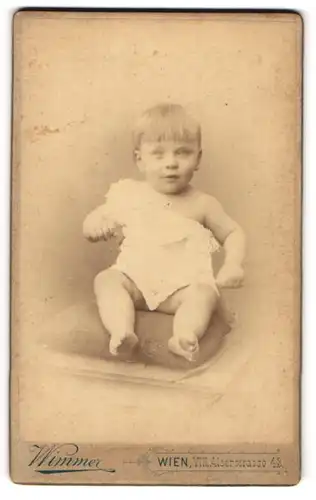 Fotografie Wimmer, Wien, Portrait niedliches Kleinkind im weissen Hemd auf Kissen sitzend