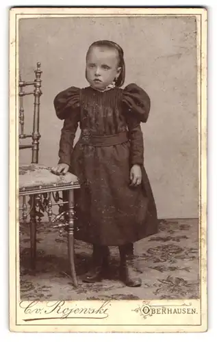Fotografie C. von Rojewski, Oberhausen a / R., Portrait kleines Mädchen im hübschen Kleid an Stuhl gelehnt