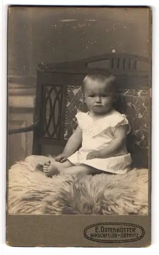 Fotografie E. Ostenkötter, Hirschfelde-Ostritz, Portrait niedliches Kleinkind im weissen Hemd auf Fell sitzend