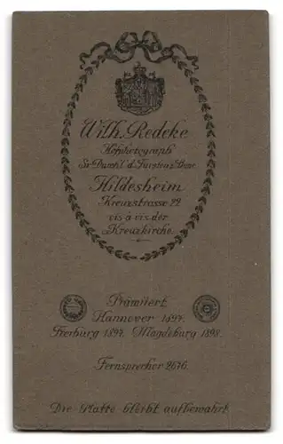 Fotografie Wilh. Redeke, Hildesheim, Portrait niedliches Kleinkind im hübschen Kleid auf Bank sitzend