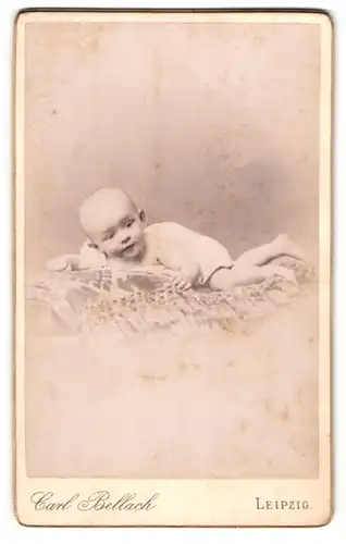 Fotografie Carl Bellach, Leipzig, Portrait niedliches Baby im weissen Hemd auf Decke liegend