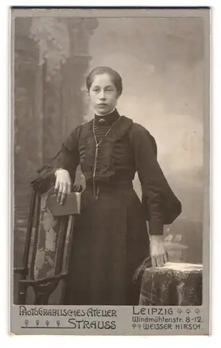 Fotografie Atelier Strauss, Leipzig, Portrait junge Dame im schwarzen Kleid mit Buch an Stuhl gelehnt