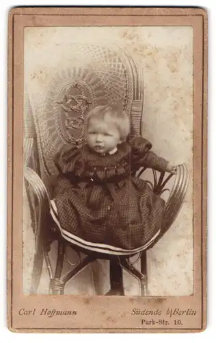 Fotografie Carl Hoffmann, Berlin-Südende, Portrait neidliches Kleinkind im karierten Kleid auf Stuhl sitzend