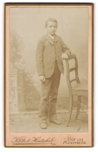 Fotografie Klotz & Hentschel, Hof, Portrait kleiner Junge im Anzug an Stuhl gelehnt