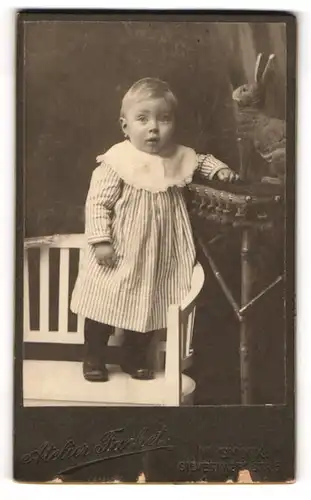 Fotografie Atelier Fachet, Wien, Portrait niedliches Kleinkind im gestreiften Kleid auf Bank sitzend
