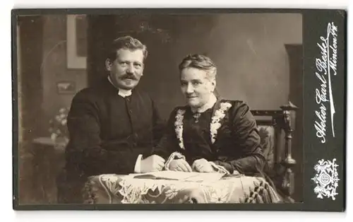 Fotografie Carl Beste, Minden i / W., Portrait bürgerliches Paar mit Buch am Tisch sitzend