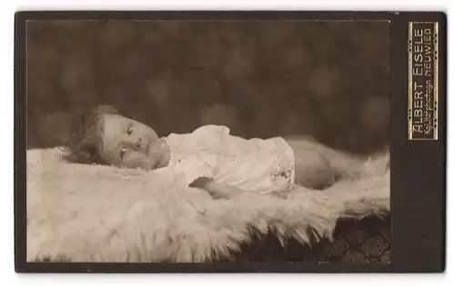 Fotografie Albert Eisele, Neuwied, Portrait niedliches Kleinkind im weissen Hemd auf Fell liegend