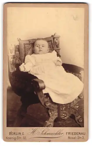 Fotografie H. Schmuckler, Berlin, Portrait niedliches Baby im weissen Kleid auf Stuhl sitzend