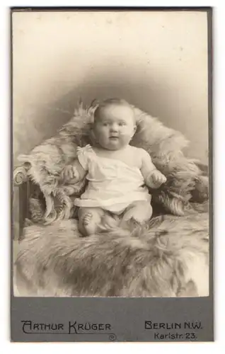 Fotografie Arthur Krüger, Berlin-NW, Portrait niedliches Baby im weissen Hemd auf Fell sitzend