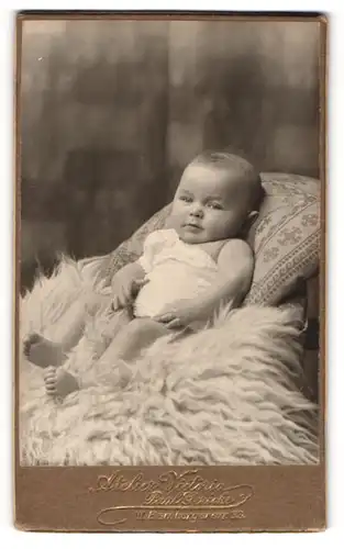 Fotografie Paul Gericke, Berlin, Portrait niedliches Baby im weissen Hemd auf Fell liegend