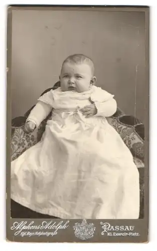 Fotografie Alphons Adolph, Passau, Portrait niedliches Baby im weissen Kleid auf Sessel sitzend