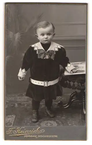 Fotografie Franz Heinrich, Torgau, Portrait niedliches Kleinkind in hübscher Kleidung mit Buch an Hocker gelehnt