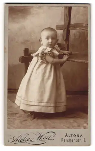 Fotografie Atelier Weil, Hamburg-Altona, Portrait niedliches Kleinkind im hübschen Kleid an Bank gelehnt