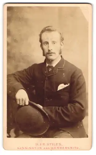 Fotografie H. & R. Stiles, Kensington-W, Portrait modisch gekleideter Herr mit Hut in der Hand