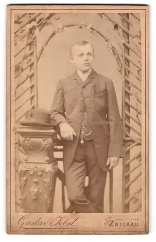 Fotografie Gustav Jobst, Zwickau, Portrait junger Mann im Anzug mit Hut an Sockel gelehnt