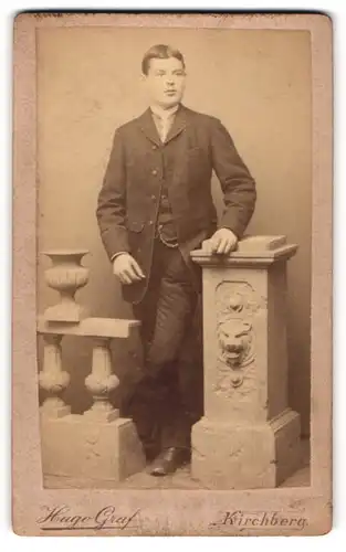 Fotografie Hugo Graf, Kirchberg, Portrait junger Mann im modischer Kleidung an Sockel gelehnt