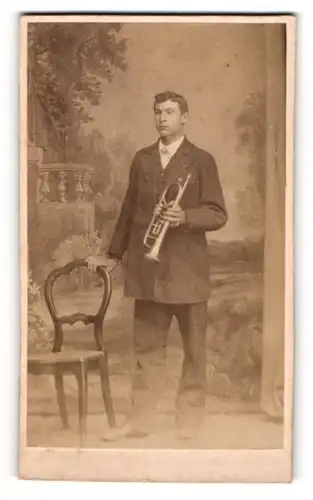 Fotografie unbekannter Fotograf und Ort, junger Mann als Musiker mit Trompete vor einer Studiokulisse