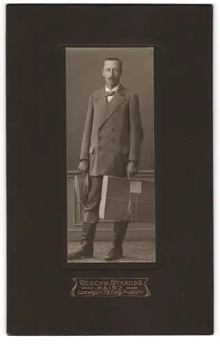 Fotografie Geschw. Strauss, Mainz, junger Mann im Anzug mit Packet in der Hand, Lederstiefel